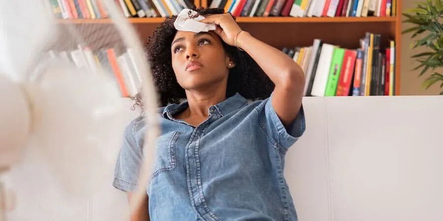 woman sitting in front of fan wiping forehead